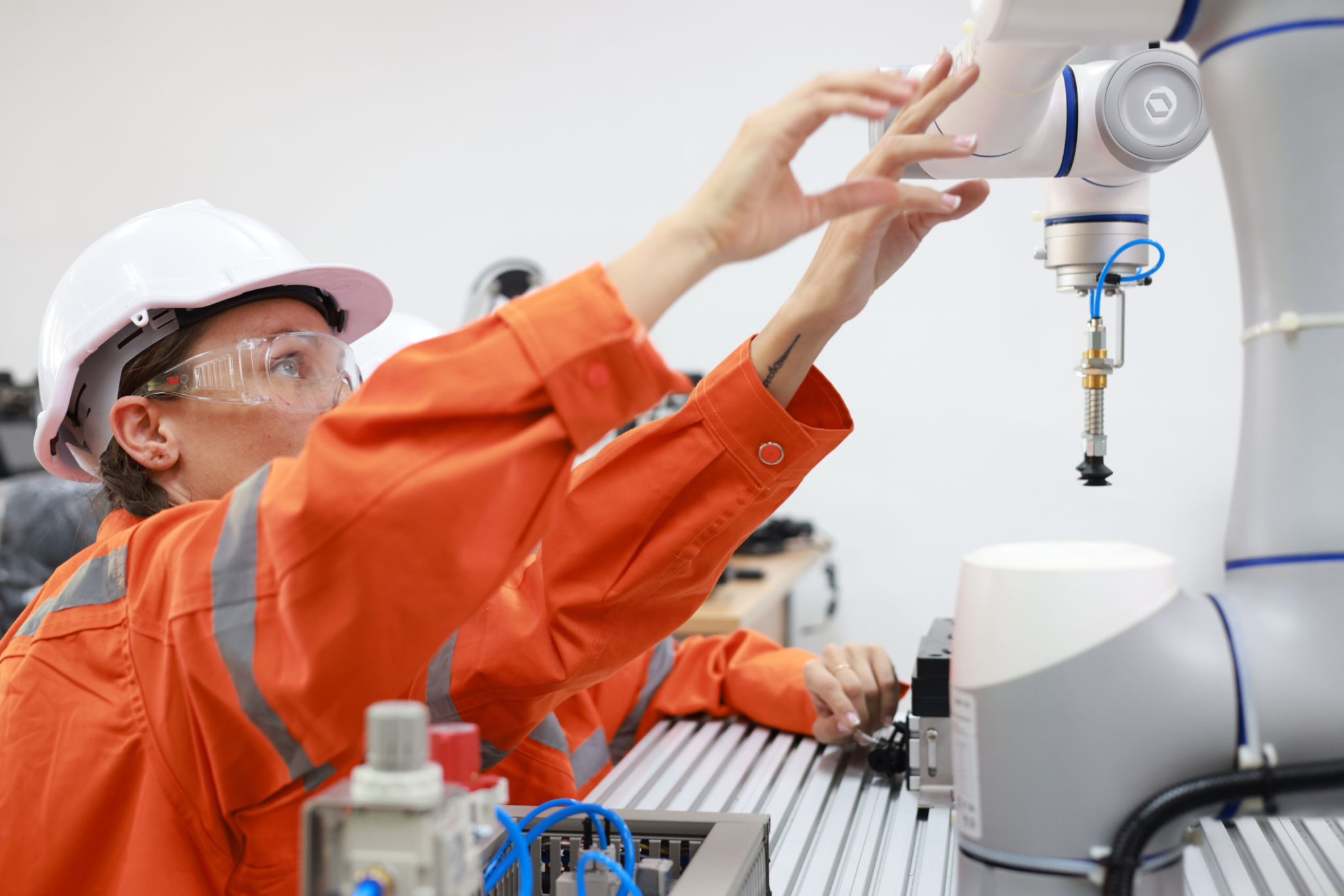 Women robotics engineers team working on project research, examining a robot arm prototype and programming it.